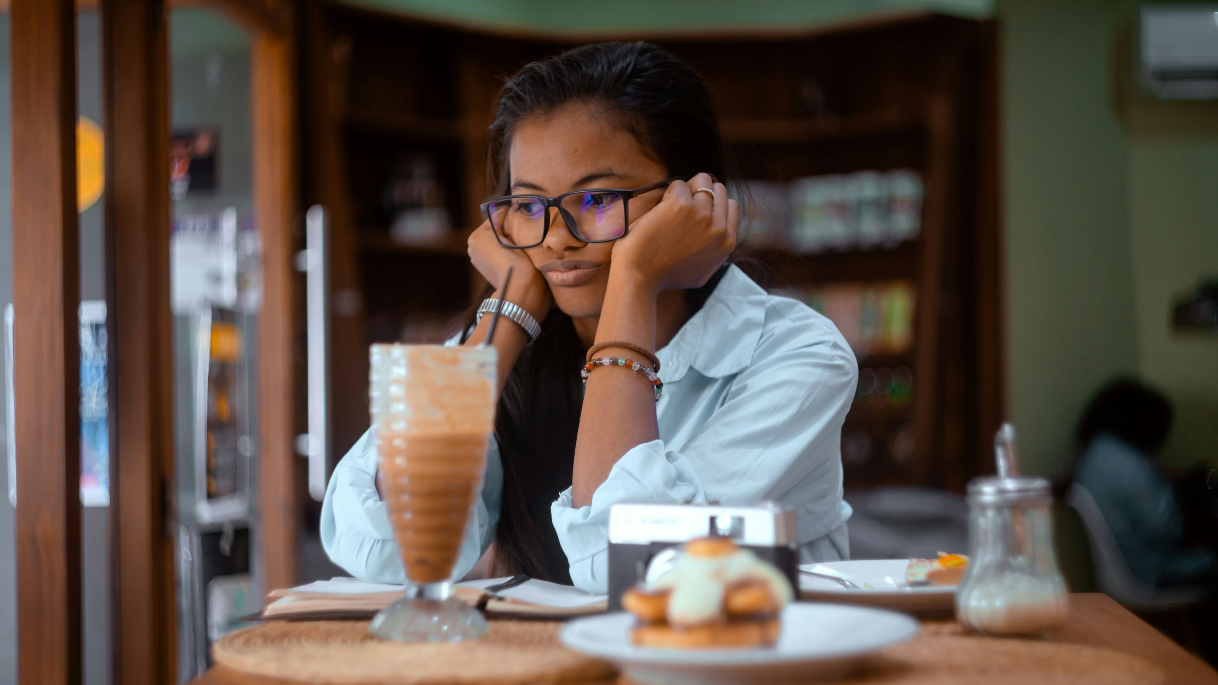 A woman sitting at a table with a drink in front of her - Photo by Shane Ryan Herilalaina on Unsplash